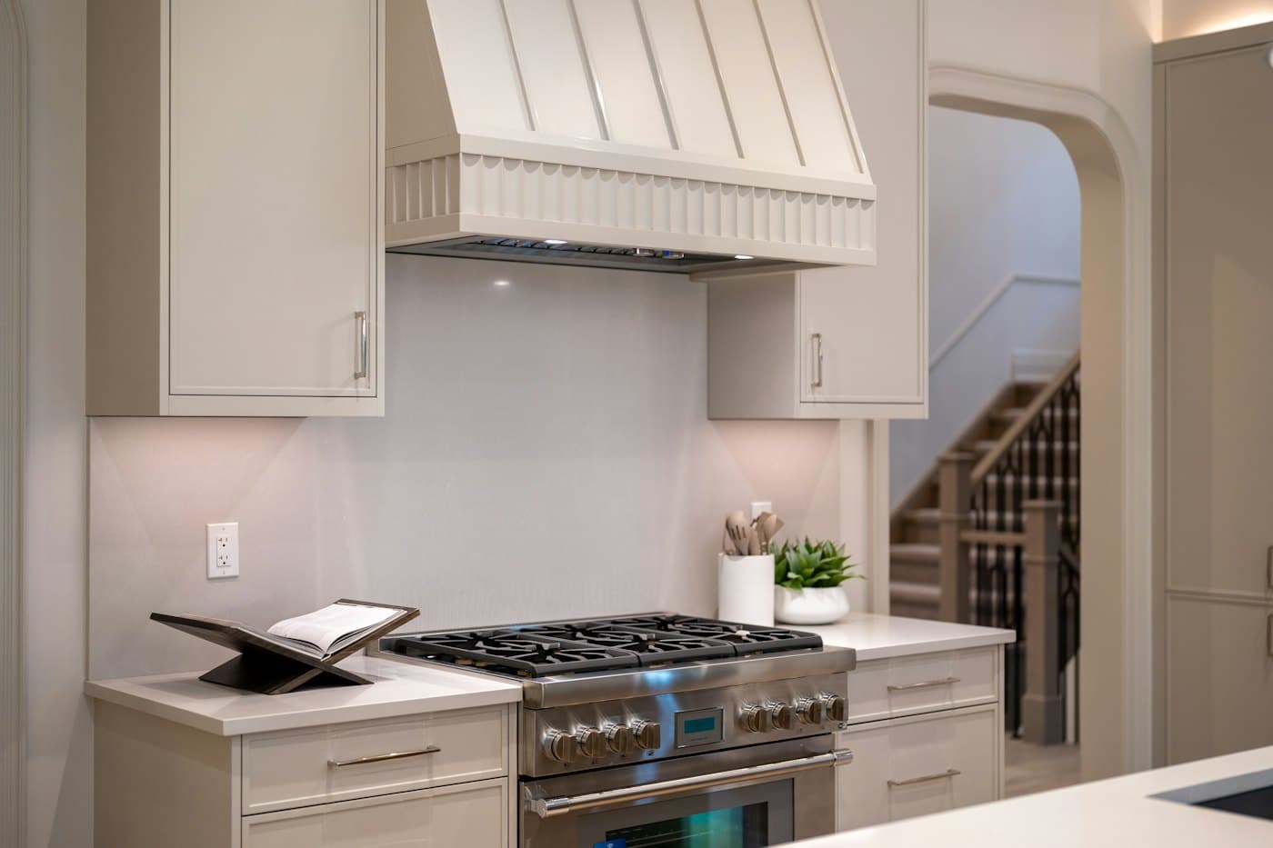 A white kitchen with a stainless steel range and hood
