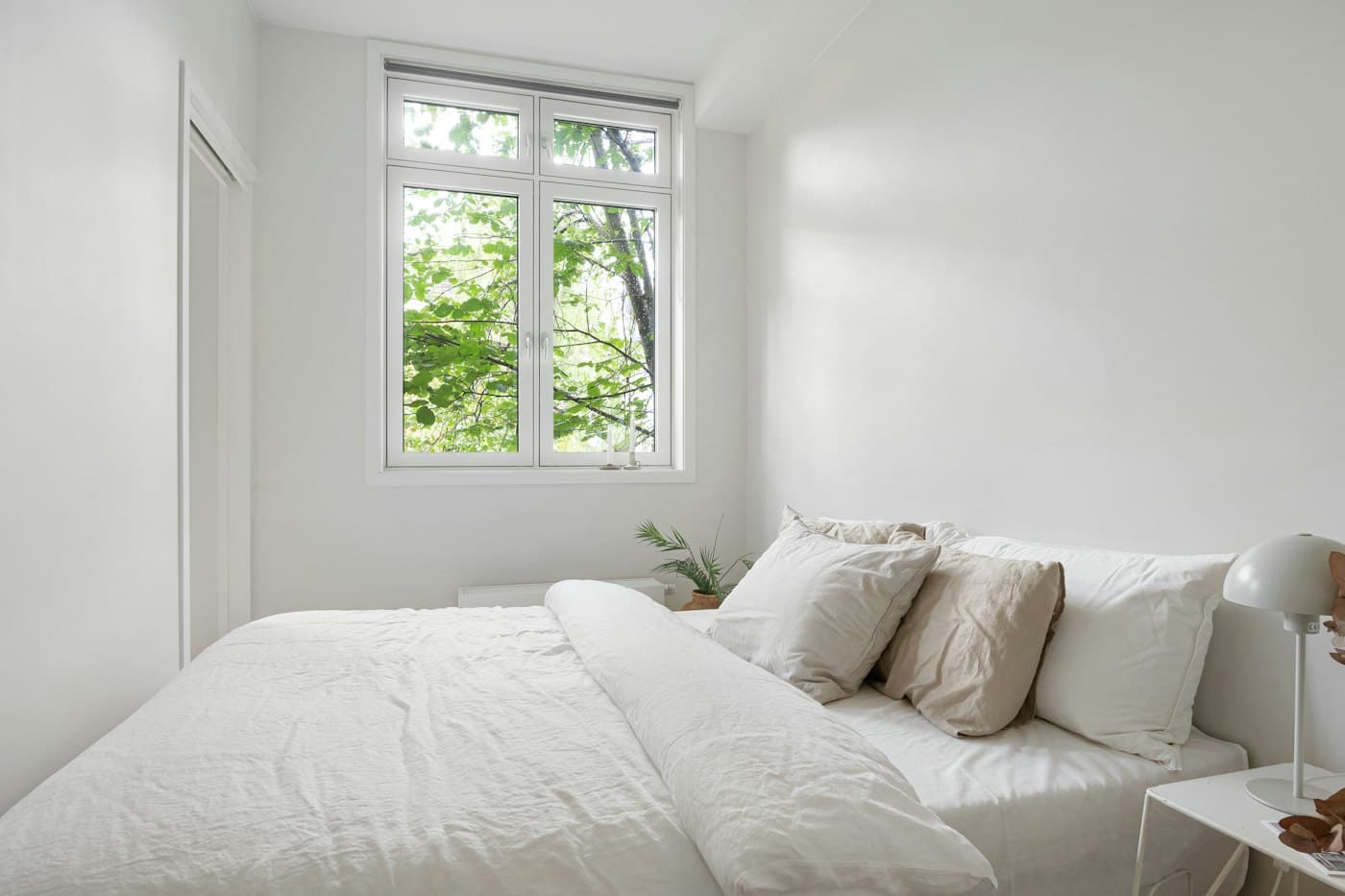 A calm bedroom with a neatly made white bed beside a window
